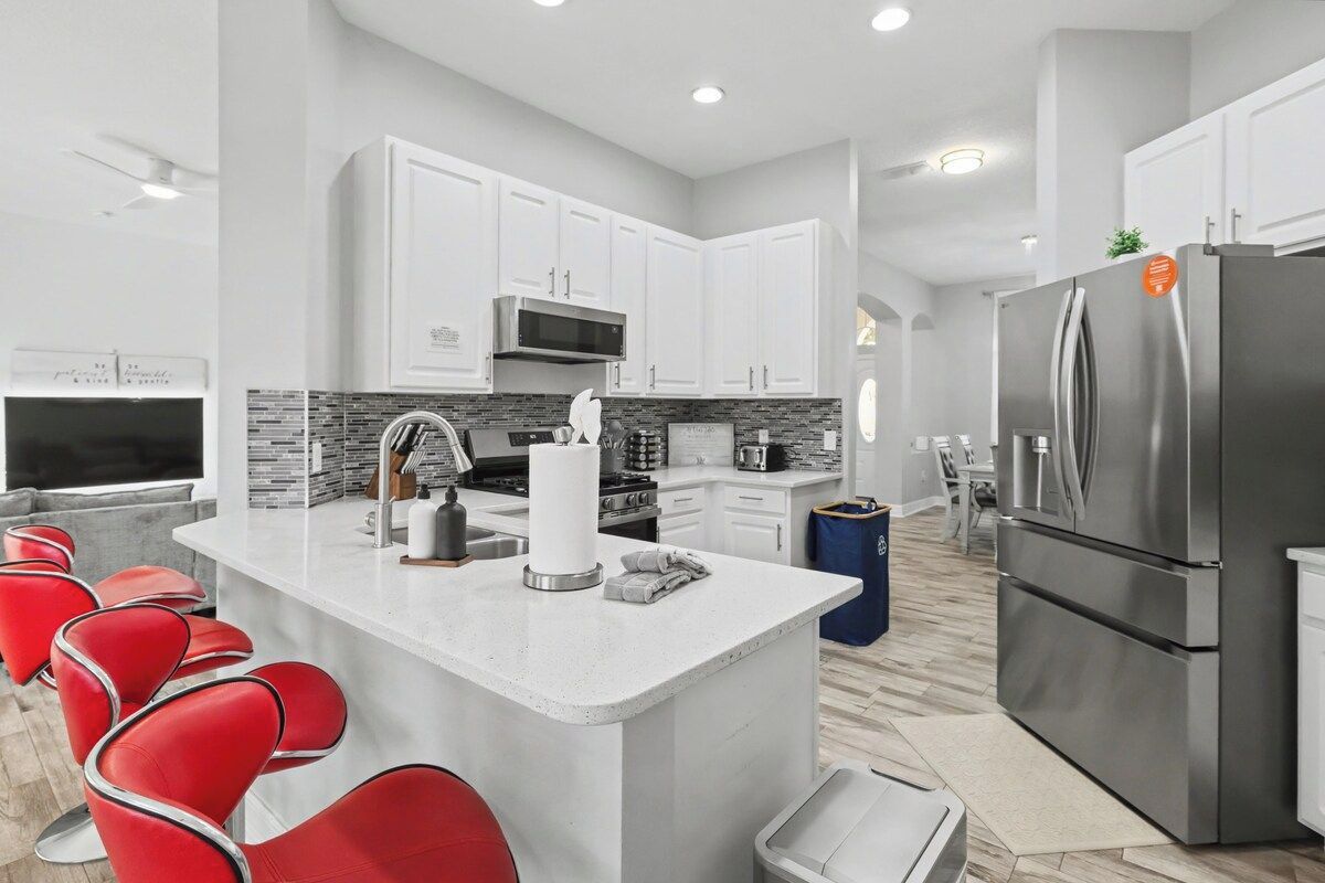 A modern kitchen with white cabinets, a stainless steel refrigerator, and a central island with seating.