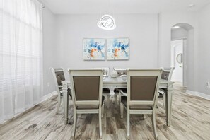 A dining room with a white table, four chairs, and two abstract paintings on the wall. - 5BR Pool Home Near Disney (Kissimmee)