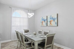 Ein Esszimmer mit einem rechteckigen Tisch, gedeckt für vier Personen, umgeben von Stühlen, einer Chandelierleuchtre und Kunstwerken an der Wand.