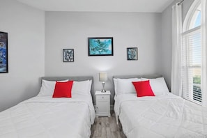 Ein Hotelzimmer mit zwei Betten, einem Nachttisch mit Lampe und gerahmten Kunstwerken an der Wand.