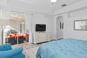 A bedroom with a bed, a TV, a dresser, and a balcony with outdoor furniture. - 5BR Pool Home Near Disney (Kissimmee)