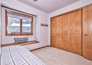 Une chambre à coucher avec un lit, une fenêtre donnant sur un beau paysage, une armoire en bois et un banc avec un coussin.