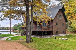 A cabin with a deck, surrounded by trees and a lake. - Sleeps 22 Private Secluded Beach Lake Home on Eagle River Chain Of Lakes! (Eagle River)