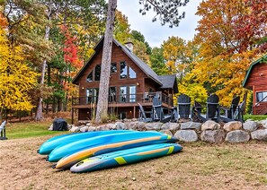 Eine Hütte mit Terrasse, umgeben von Herbstbäumen, und mehrere Kajaks, die davor angeordnet sind.