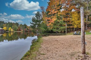 A lakeside view with a sandy beach, trees with autumn foliage, and a clear sky. - Sleeps 22 Private Secluded Beach Lake Home on Eagle River Chain Of Lakes! (Eagle River)