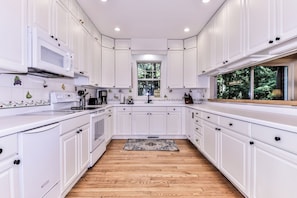 A modern kitchen with white cabinetry, a wooden floor, and a window providing a view of greenery. - Nestled on the banks of East Bay Little Saint Germain Lake! (St Germain)