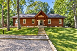 A wooden cabin with a front porch, surrounded by trees and a gravel pathway leading to the entrance. - Nestled on the banks of East Bay Little Saint Germain Lake! (St Germain)