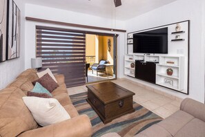 A living room with a sofa, a coffee table, a television, and a sliding door leading to an outdoor area. - Beachfront Princesa Condo: Ocean View, Pool & (Puerto Peñasco)
