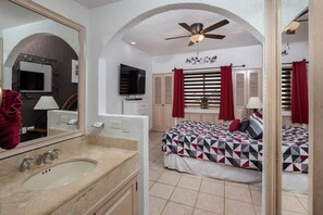 A hotel room with a large mirror, a ceiling fan, a bed with a geometric-patterned bedspread, and a window with red curtains. - Beachfront Princesa Condo: Ocean View, Pool & (Puerto Peñasco)