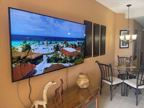 A flat-screen TV mounted on a wall displaying a tropical beach scene. - Beachfront Condo w/ Sea View, Pools, Resort Access (Puerto Peñasco)