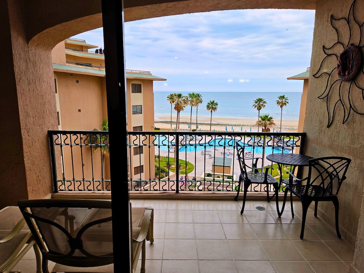 A balcony with a view of a beach and a pool.