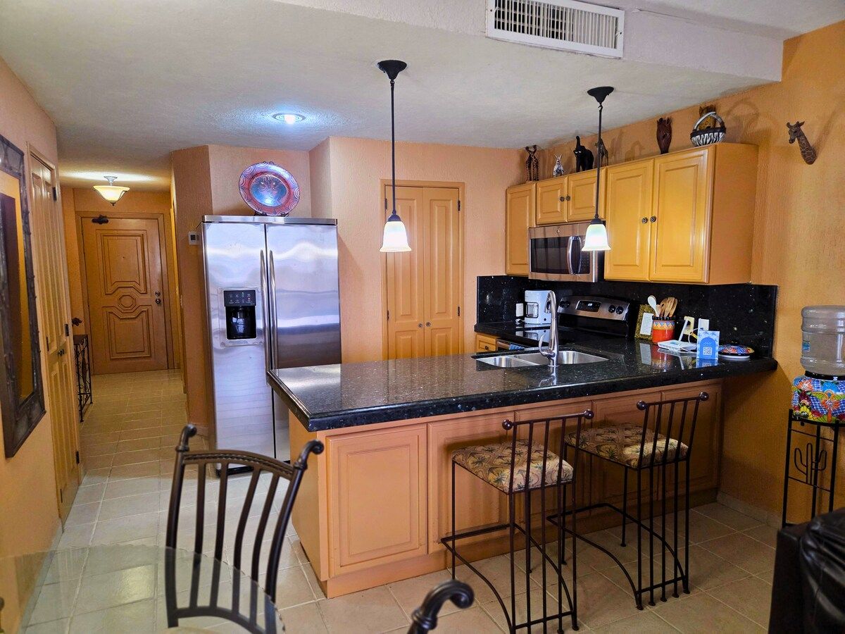 A kitchen with a central island, bar stools, a refrigerator, a microwave, and a water dispenser.