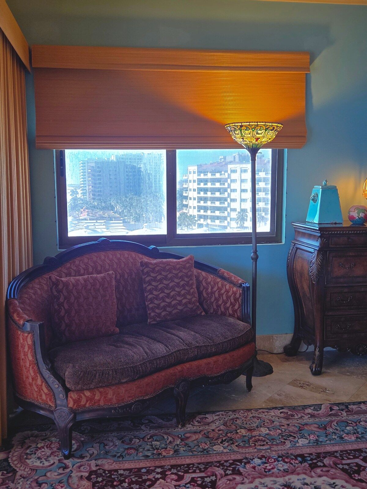 Ein Zimmer mit einer Couch, einer Lampe, einem Schminktisch und Blick auf Gebäude durch ein Fenster.