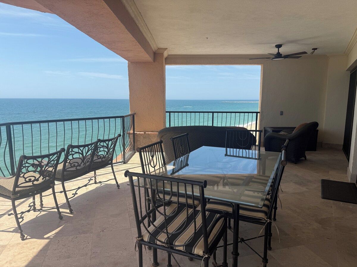 A balcony with a glass table and chairs, overlooking the sea.