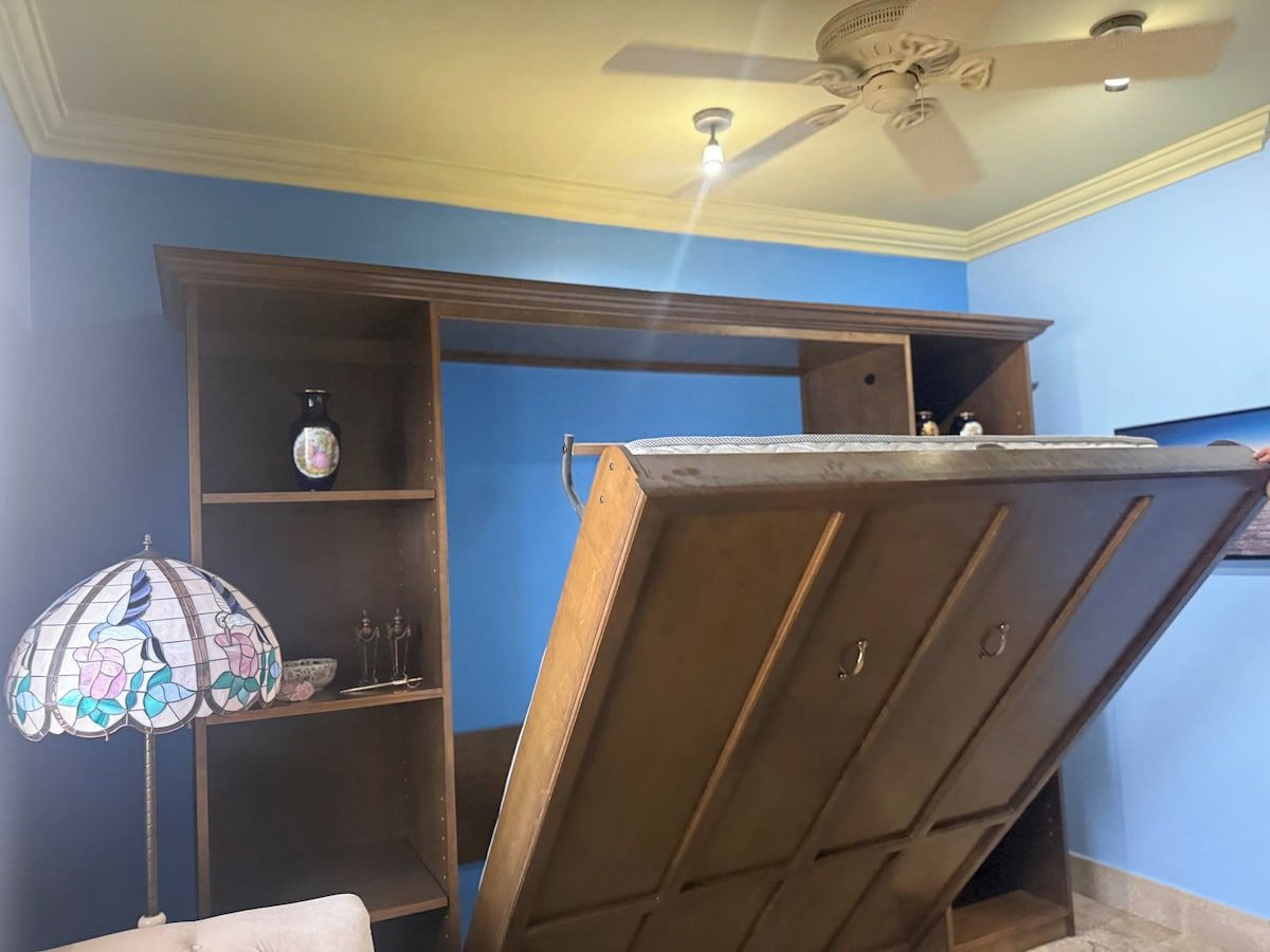 Ein Zimmer mit Deckenventilator, Holzschrank und einer Stubenlampe aus Buntglas.