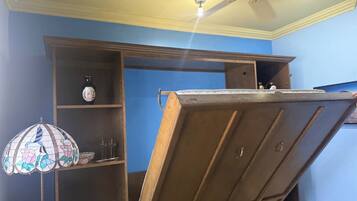 Ein Zimmer mit Deckenventilator, Holzschrank und einer Stubenlampe aus Buntglas.