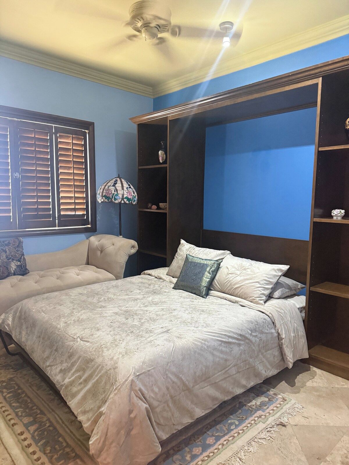 A bedroom with a bed, a nightstand, a dresser, a window with blinds, and a ceiling fan.