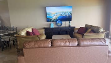 A living room with a brown leather sofa, a television mounted on the wall, and a dining area with a table and chairs.