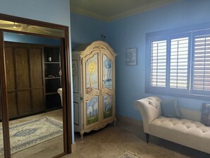 Una habitación con un sofá, un armario con puertas pintadas, una ventana con persianas y una puerta que da a otra habitación.
