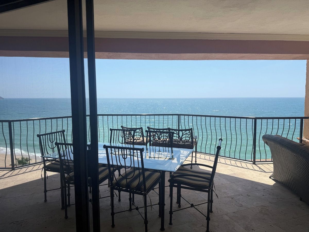 Een balkon met een tafel en stoelen, met uitzicht op een wateroppervlak.