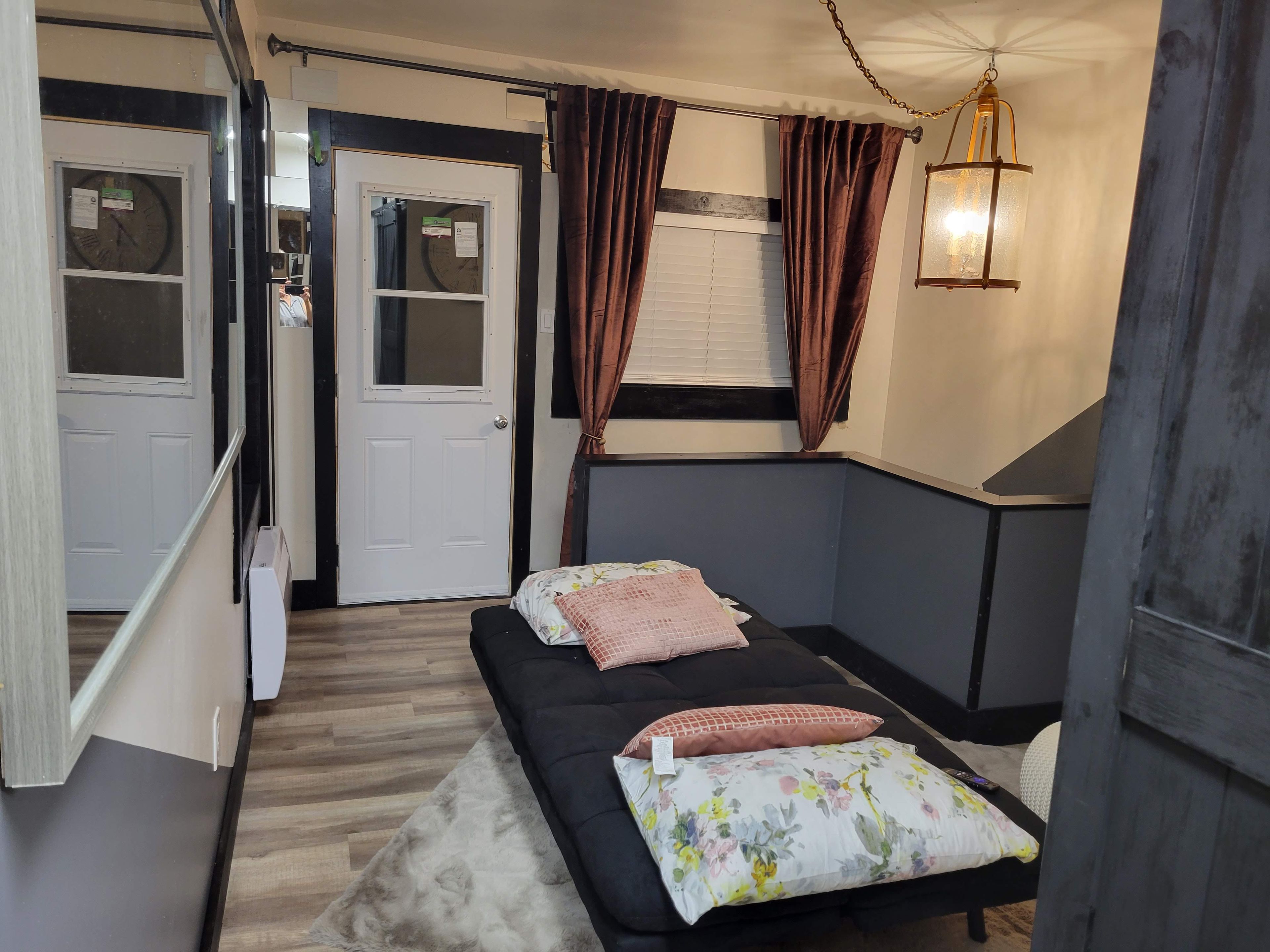 A bedroom with a bed, a window with curtains, a wall-mounted light fixture, and a door.