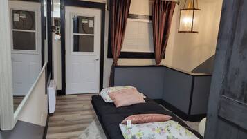 A bedroom with a bed, a window with curtains, a wall-mounted light fixture, and a door.