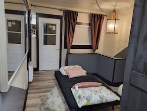Une chambre à coucher avec un lit, une fenêtre avec des rideaux, un luminaire fixé au mur et une porte.