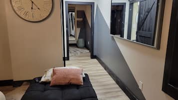 A room with a bed, a wall clock, a mirror, and a hallway leading to another room.