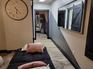 Quarto com cama, relógio de parede, espelho e corredor que dá para outro cômodo.