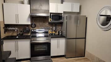 A compact kitchen with white cabinets, a stainless steel stove, a microwave, and a refrigerator.