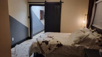 A bedroom with a bed, a ceiling fan, a window with blinds, and a door leading to another room.