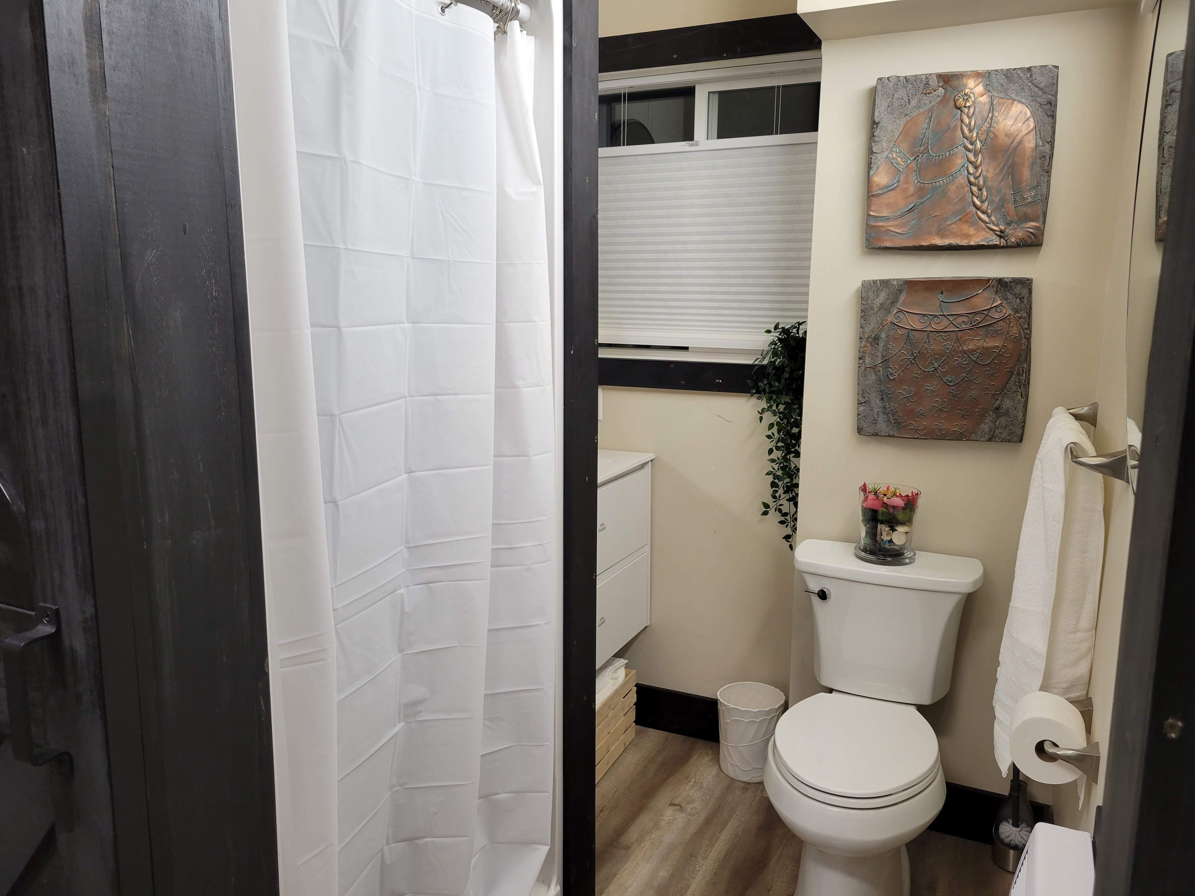 A bathroom with a white toilet, a shower curtain, and a window with blinds.