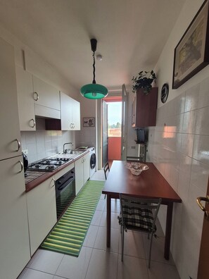 A compact kitchen with a gas stove, a washing machine, and a dining area with a table and chairs. - Cozy apartment located right near the Rescaldina train station (Rescaldina)