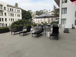 A rooftop terrace with lounge chairs, a striped umbrella, and a view of the cityscape. - Hollywood Central with Pool|Free Parking|Gym (Los Angeles)