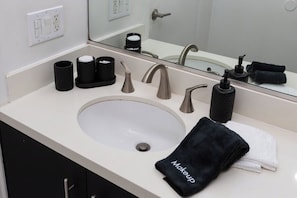Un bagno con lavandino, specchio, porta asciugamani e articoli da toilette.