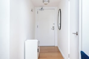 A narrow hallway with a white door at the end, a small white cabinet, and a wall-mounted circular object. - Hollywood Central with Pool|Free Parking|Gym (Los Angeles)