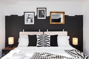 Een hotelkamer met een bed, twee nachtkastjes, een spiegel en ingelijste foto’s aan de muur.