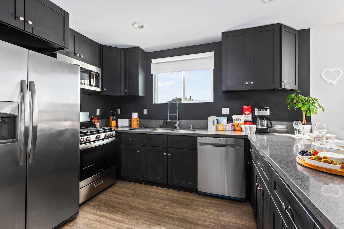 A modern kitchen with dark cabinetry, stainless appliances, and a window providing natural light.