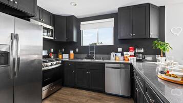 A modern kitchen with dark cabinetry, stainless appliances, and a window providing natural light.
