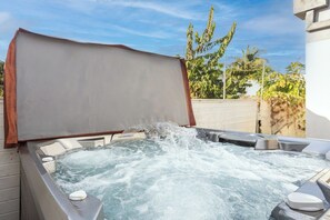 Een jacuzzi met deksel, omringd door buitenmeubels en uitzicht op groen.