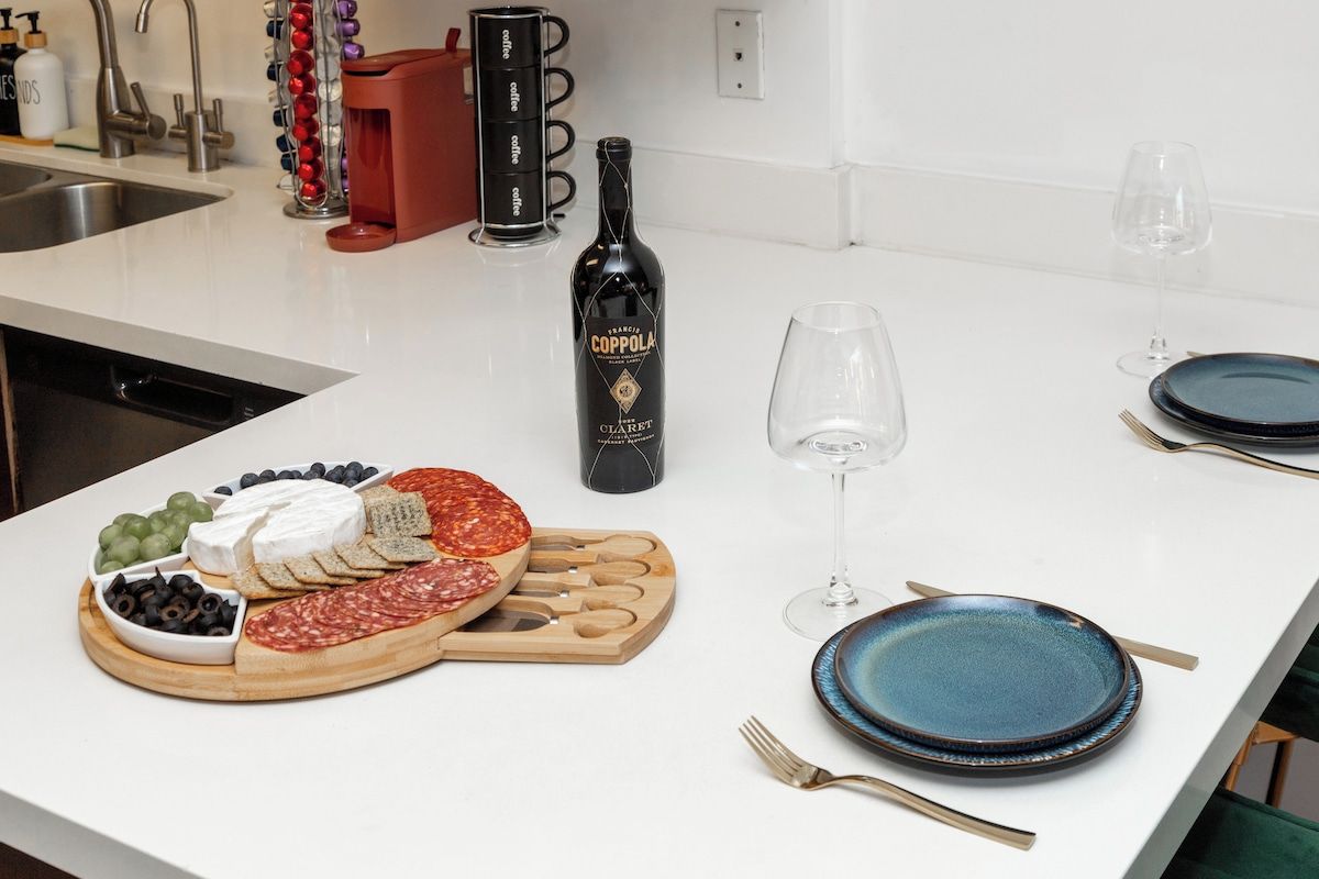 Un comptoir de cuisine avec une planche à découper pour charcuterie, une bouteille de vin et des assiettes.