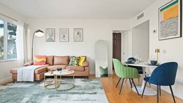 A modern living room with a sofa, coffee table, and chairs. There is a dining table with chairs and a painting on the wall.