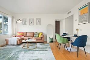 A modern living room with a sofa, coffee table, and chairs. There is a dining table with chairs and a painting on the wall. - Hollywood Central with Pool| Free Parking|Gym (West Hollywood)