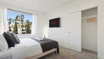 A hotel room with a bed, a TV mounted on the wall, a closet, and a window with curtains.