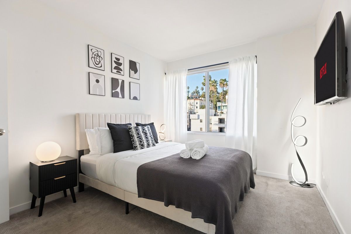 A modern bedroom with a bed, bedside table, and a TV mounted on the wall.