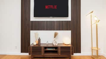 A modern living room with a mounted TV displaying 'NETFLIX', a wooden console table with decorative items, and a floor lamp.