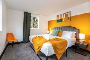 Ein Hotelzimmer mit einem Bett, einem Nachttisch, einem Sessel und einem Fenster mit Vorhängen.