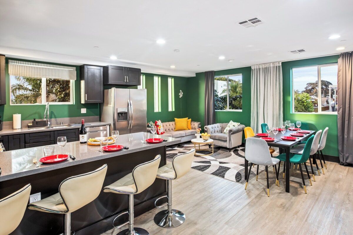 A modern kitchen with a central island, a dining area with a table set for six, and a living area with a sofa and chairs.