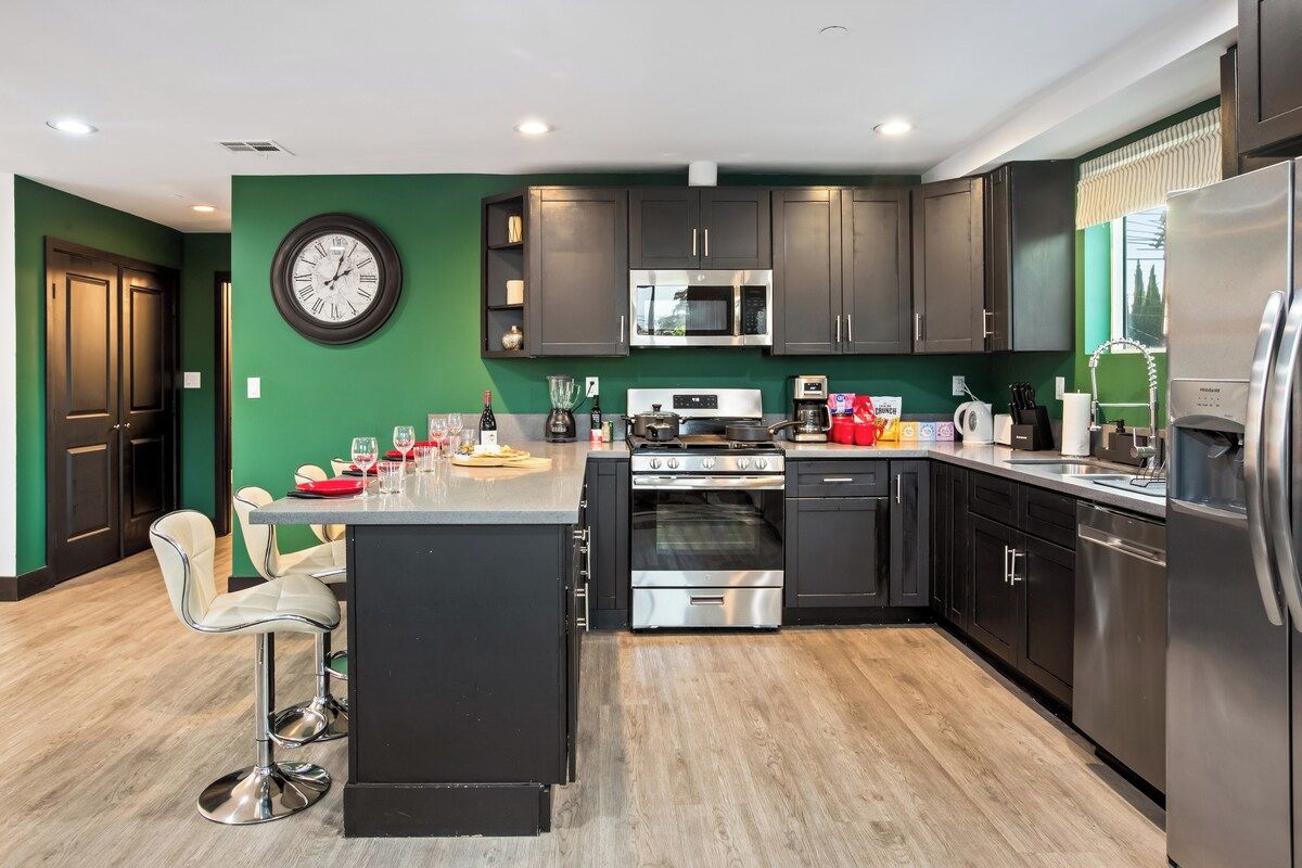 A modern kitchen with dark cabinets, stainless steel appliances, and a green accent wall.