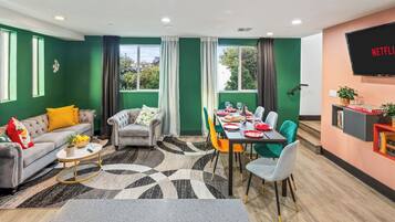 Een moderne woonkamer met een bank, fauteuil, salontafel, en een eetgedeelte met stoelen en een tafel gedekt voor een maaltijd.